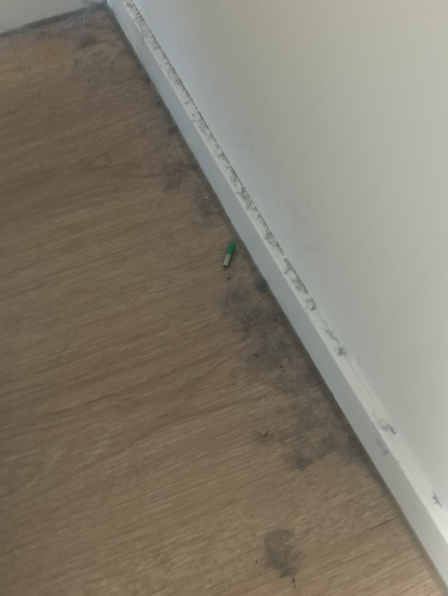 Vloer langs de plint met stof en aangekoekt vuil in de hoek, vóór de schoonmaak